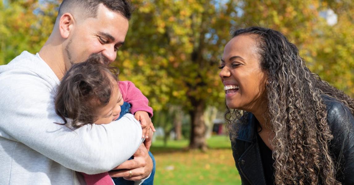 Happy looking man holding a laughing toddler while looking at a woman laughing
