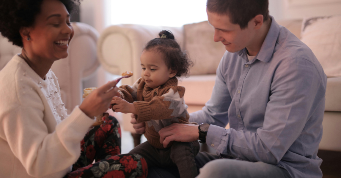 Man holding young girl while woman is feeding her